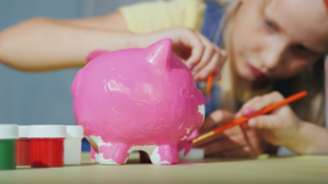 image shows children painting a ceramic money box